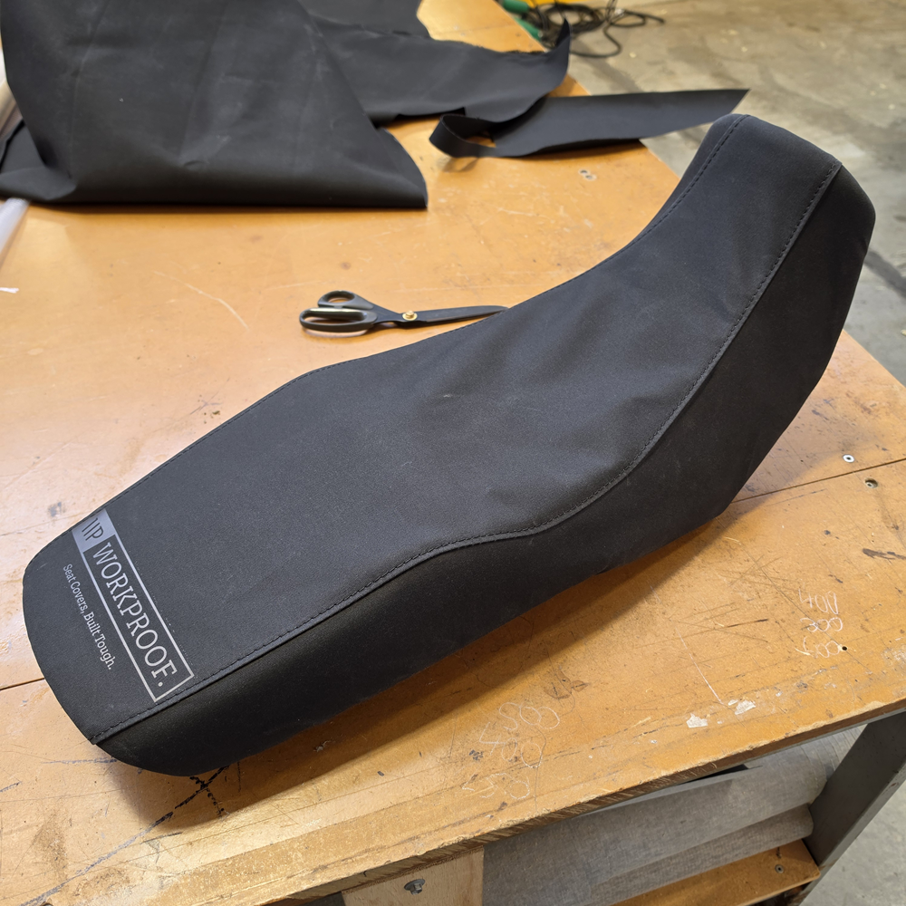 Black WORKPROOF canvas seat cover fitted to a 2026 Suzuki DR150 motorbike, heavy-duty waterproof protection with a secure custom fit for farm and trail riding.